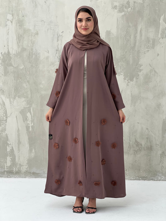 A woman wearing a Cinnamon Brown Chiffon Abaya with floral patterns and a matching brown headscarf.