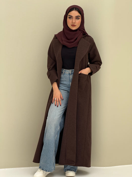 a woman wearing a dark brown Coat style abaya with lapel collar, Contrast black buttons, large patch pockets, cuff straps and matching sheila