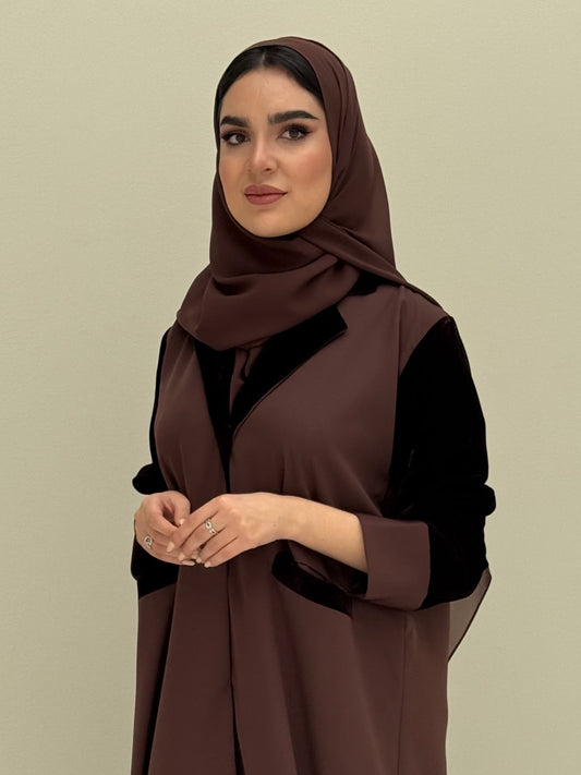A woman wearing a dark brown abaya with velvet and barbei fabric, posing against a neutral background.