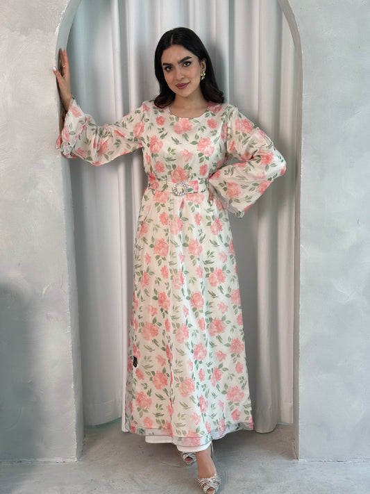 A woman wearing a White & Pink Blossom printed organza (Lined) jalabiya dress with long sleeves and a belt, standing in front of a neutral backdrop.