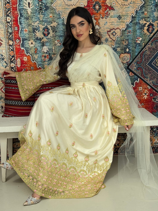 A woman sitting in front of a colorful backdrop wearing a cream and gold-colored Saree-Style Draped Jalabiya with net embroidery, featuring a belt.