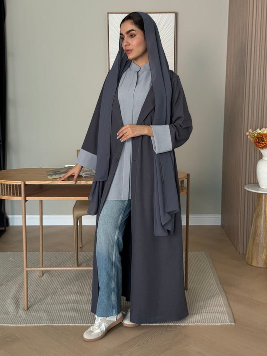A woman wearing a long Light Grey Linen Coat Abaya with a matching sheila headscarf in a room.
