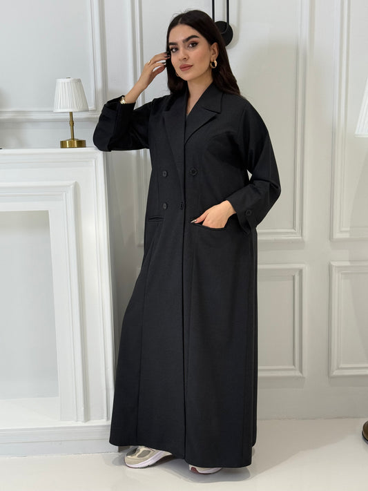 Woman wearing a long Black Jookh Abaya Set standing in front of a white door.