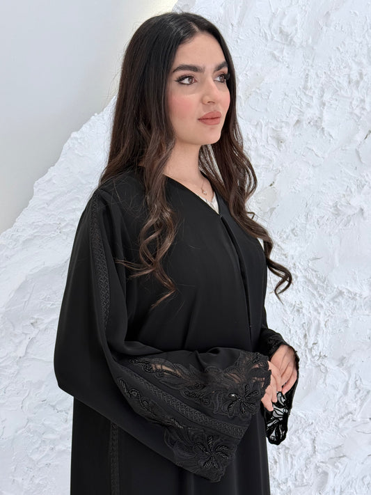 Person wearing a Premium Luxury Hand-Embellished Black Abaya outfit made from Nida fabric, standing on a textured white surface