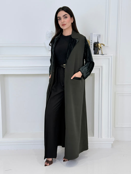 Woman wearing a long olive green coat-style abaya made from Premium Barbie (Body) and Crushed Velvet in a white interior setting