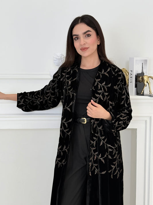 Person wearing a Premium Velvet Abaya with Gold Vine floral Embroidery patterns in a room with white walls.