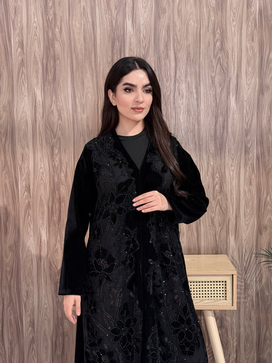 woman wearing a Premium Black Velvet Abaya with Floral Embroidery, lace garment on a wooden floor background