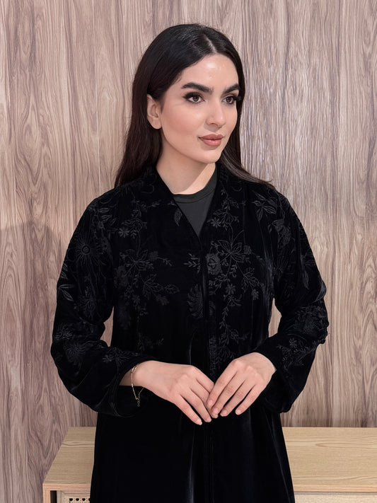 Woman wearing a Premium Black Velvet Abaya with Floral Embroidery on a wooden floor.