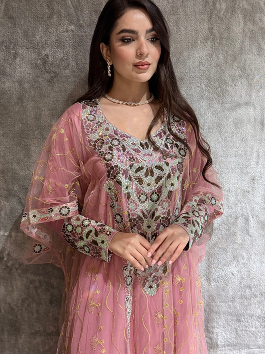 Woman wearing a dusty pink Embroidered Authentic Emirati Thobe-inspired Design jalabiya against a gray textured wall.