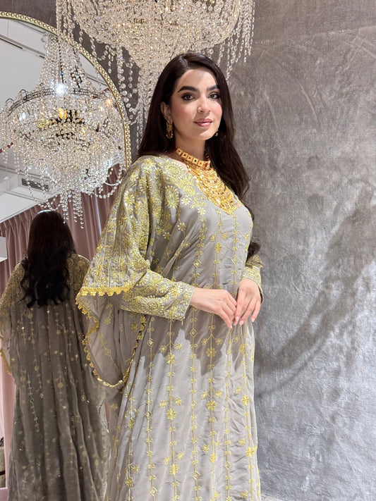 Woman in a Grey Luxury Embroidered Kaftan Dressstanding in front of a textured wall.
