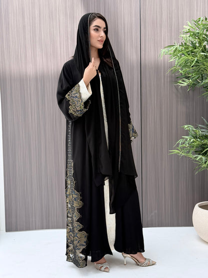 Woman wearing a black abaya with floral embroidery in a minimal indoor setting.