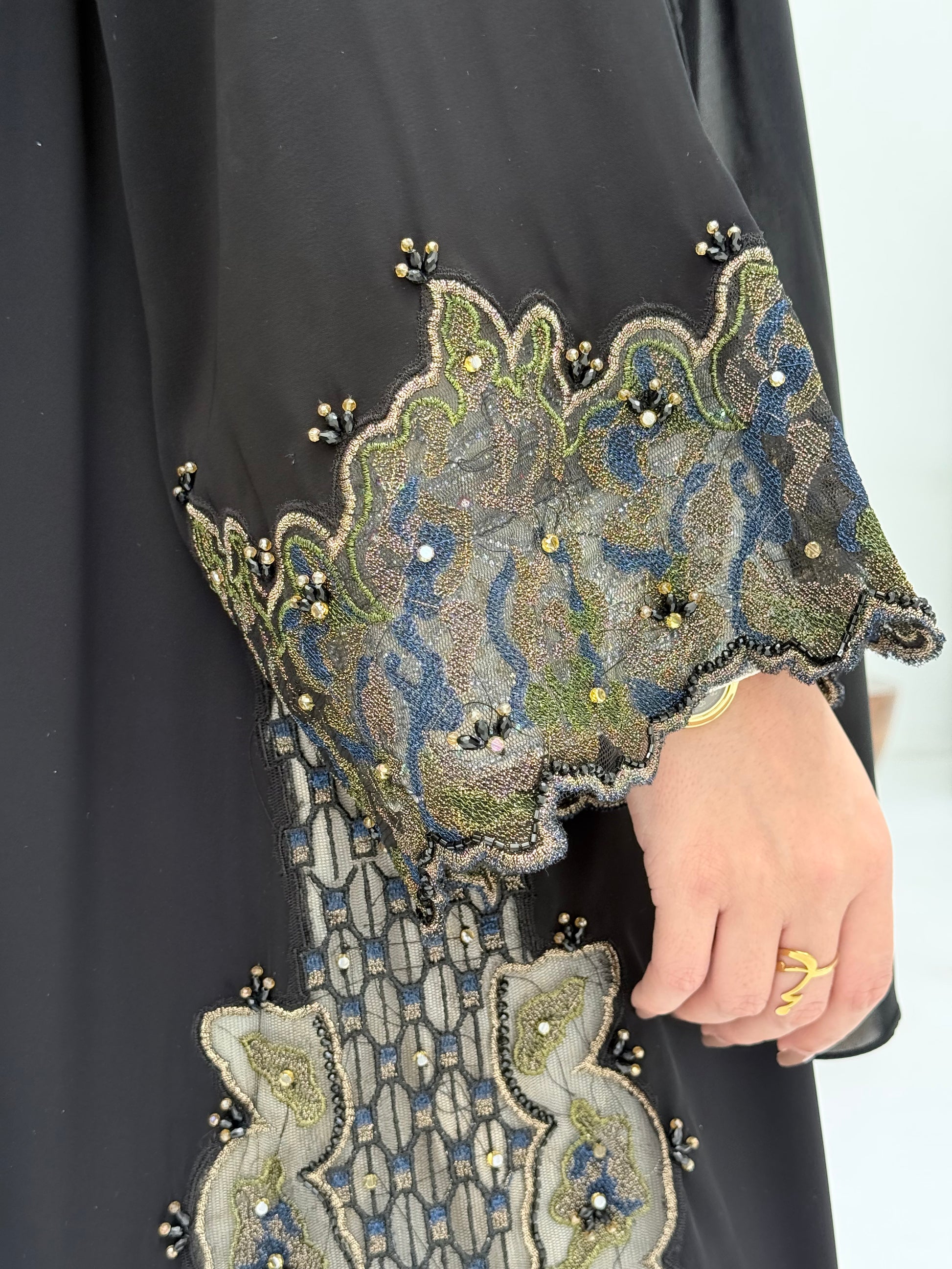 close up of a woman wearing an elegant open-front black abaya featuring intricate multi-colored beadwork, sequins, and metallic embroidery in an indoor setting.