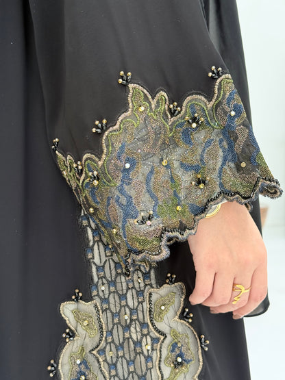 close up of a woman wearing an elegant open-front black abaya featuring intricate multi-colored beadwork, sequins, and metallic embroidery in an indoor setting.