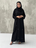 A woman wearing a black Chiffon abaya with floral patterns and a matching black headscarf.