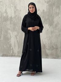 A woman wearing a black Chiffon abaya with floral patterns and a matching black headscarf.