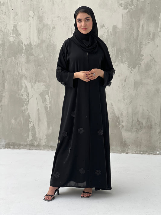 A woman wearing a black Chiffon abaya with floral patterns and a matching black headscarf.