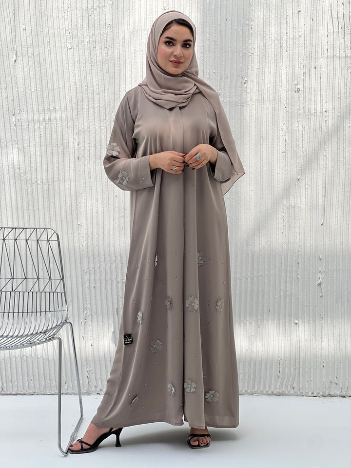 A woman wearing a Light Brown Chiffon Abaya with floral patterns and a matching brown headscarf.