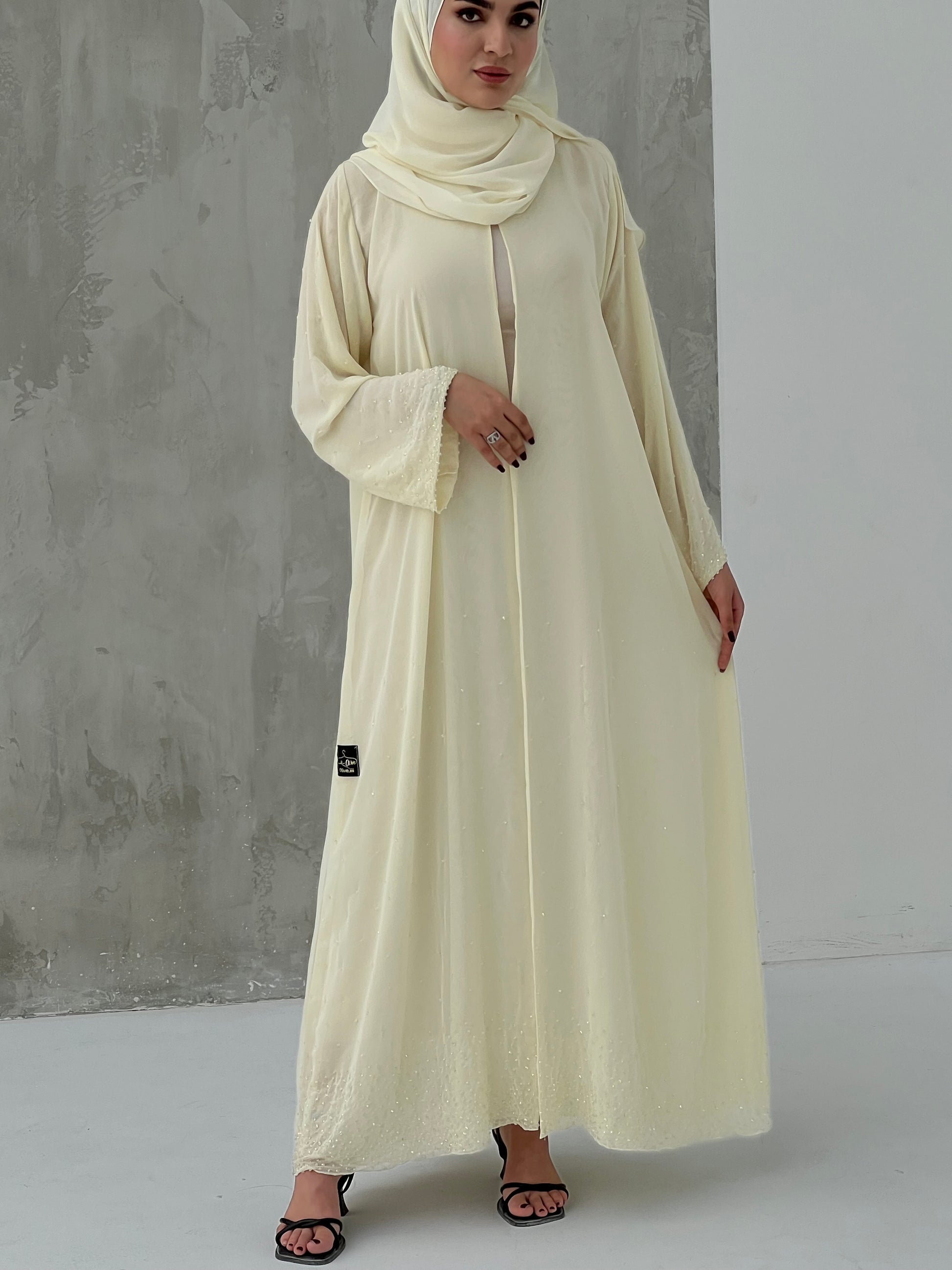 A woman wearing a Cream Chiffon Abaya with Crystal Beads with long sleeves and a matching headscarf.