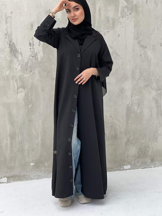 A woman wearing a Black Coat-Style Abaya with buttons down the front, paired with a matching headscarf.