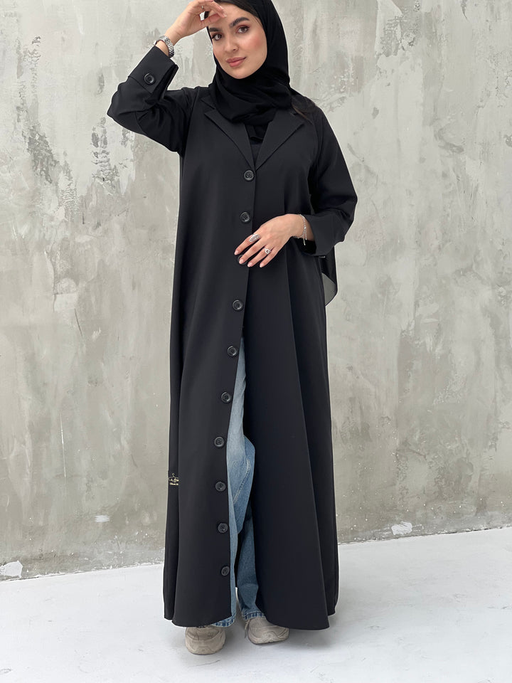 A woman wearing a Black Coat-Style Abaya with buttons down the front, paired with a matching headscarf.