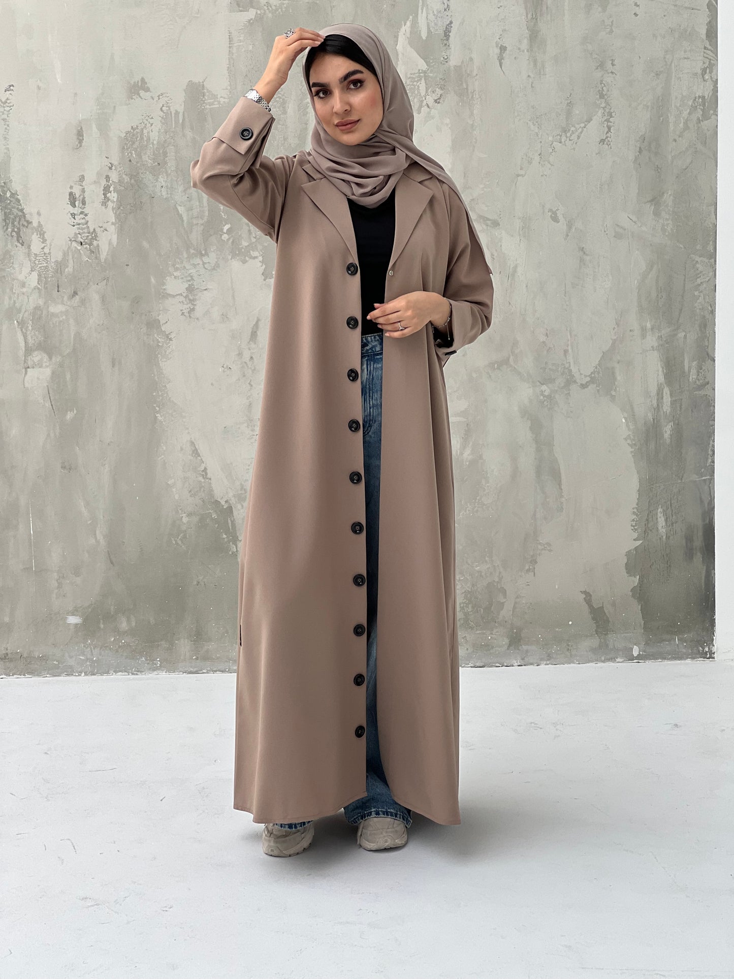 A woman wearing a Beige  Coat-Style Abaya with buttons down the front, paired with a matching headscarf.