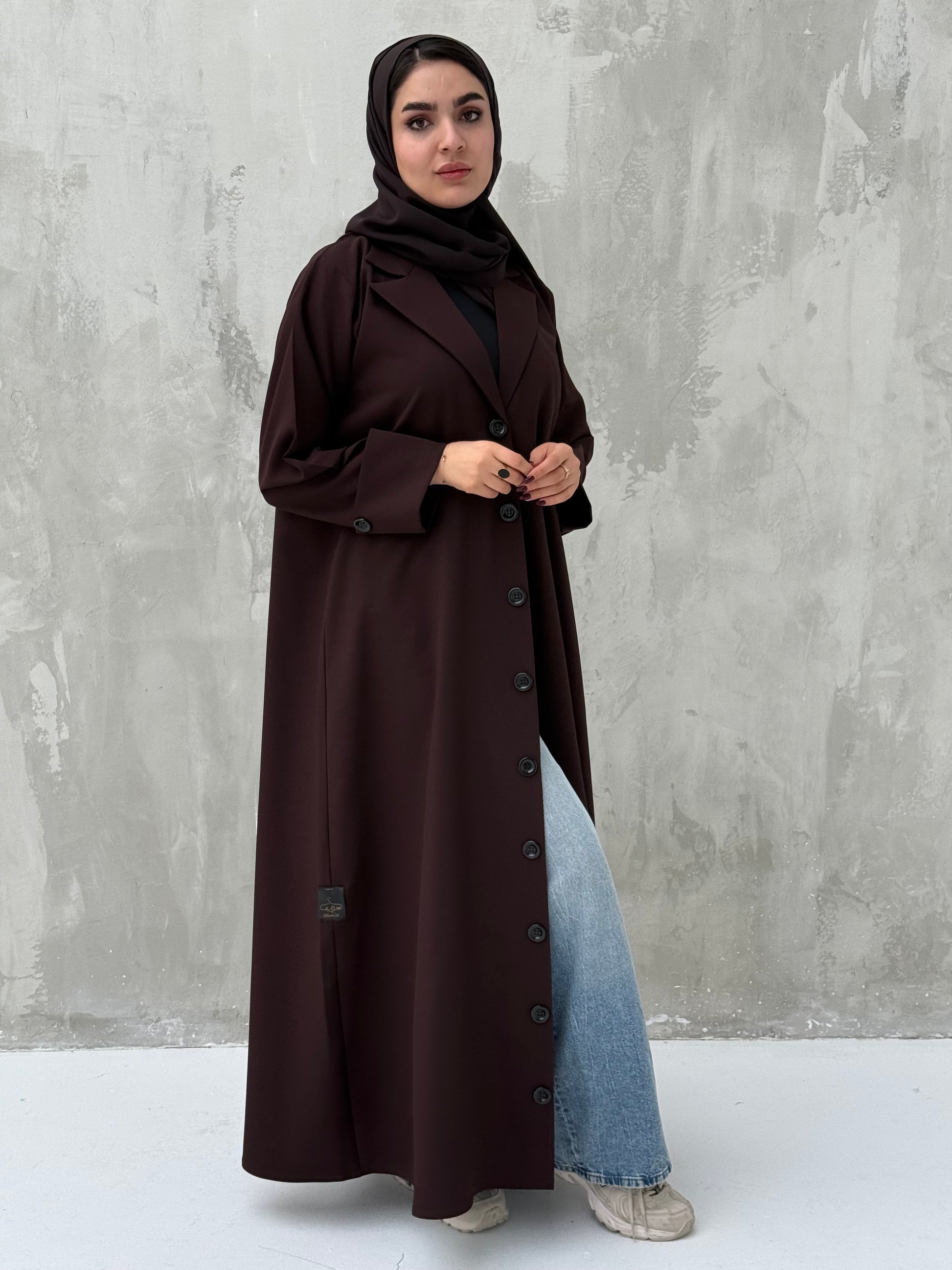 A woman wearing a Dark Brown Coat-Style Abaya with buttons down the front, paired with a matching headscarf.