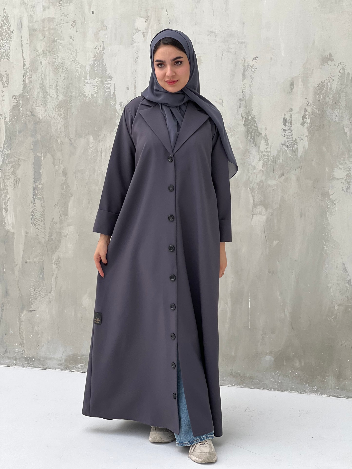 A woman wearing a Dark Grey Coat-Style Abaya with buttons down the front, paired with a matching headscarf.