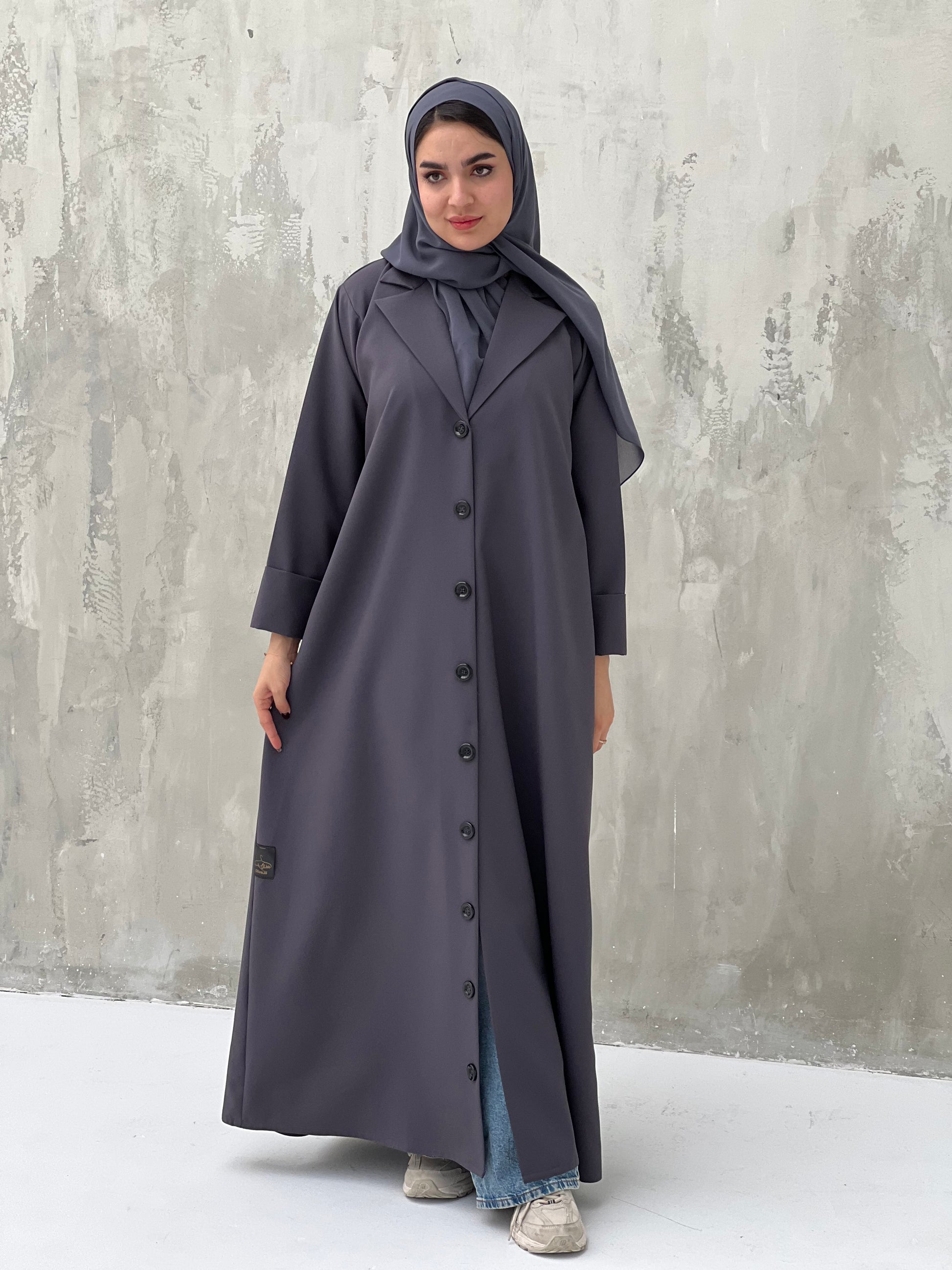 A woman wearing a Dark Grey Coat-Style Abaya with buttons down the front, paired with a matching headscarf.