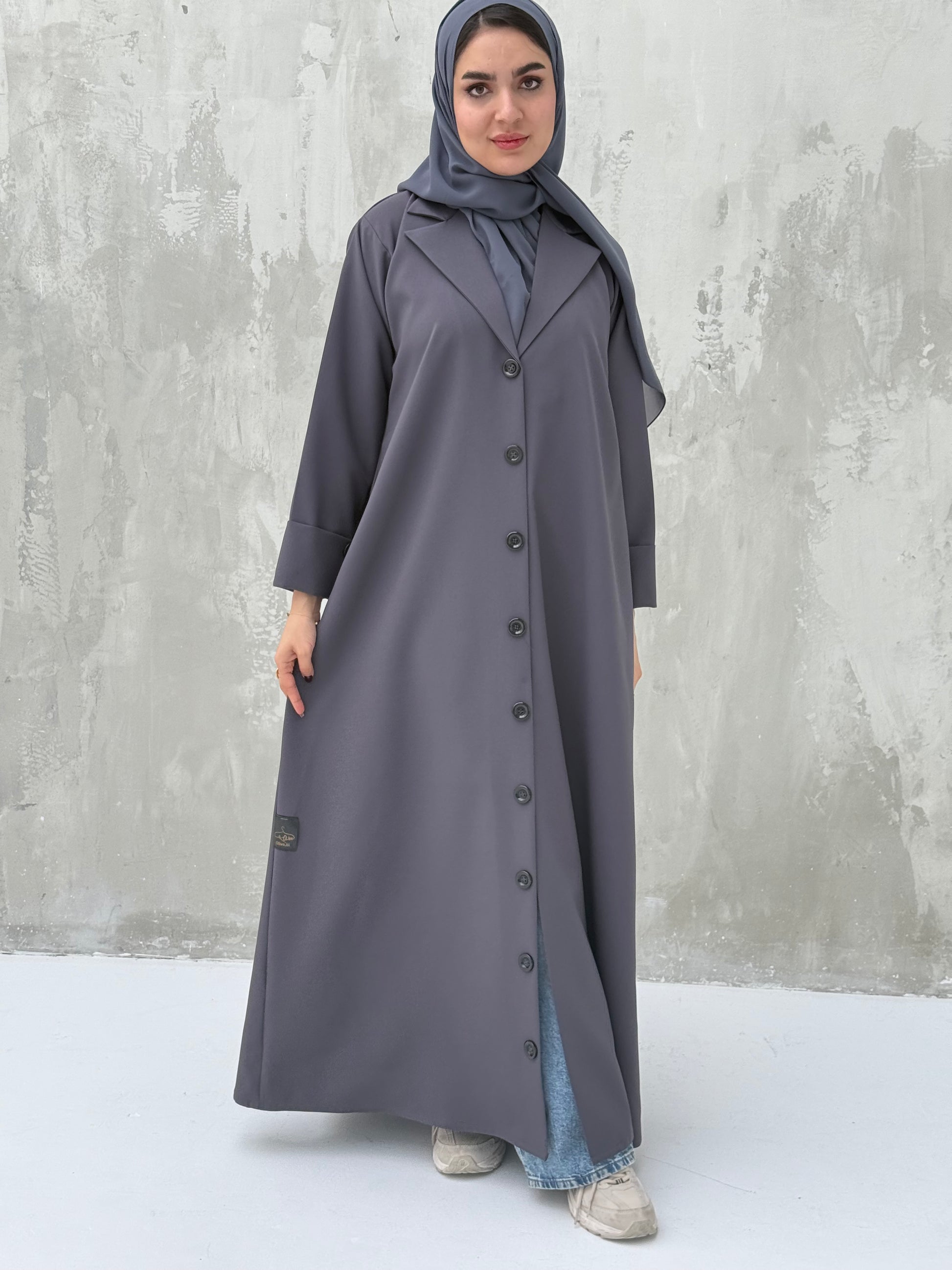 A woman wearing a Dark Grey Coat-Style Abaya with buttons down the front, paired with a matching headscarf.