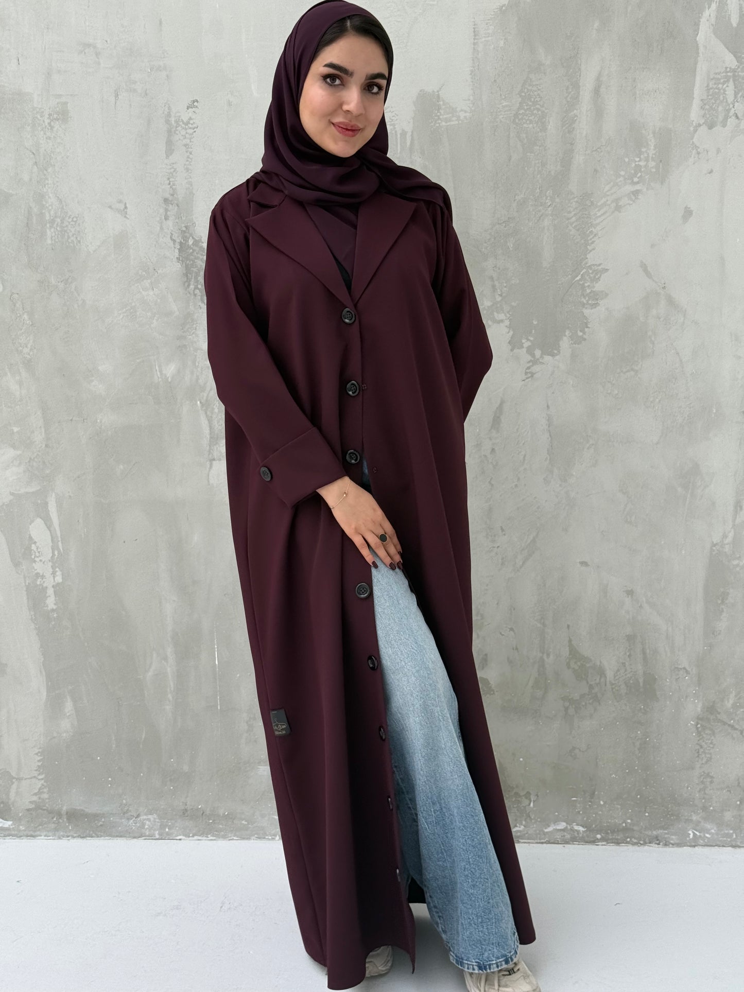 A woman wearing a Maroon Coat-Style Abaya with buttons down the front, paired with a matching headscarf.
