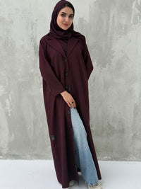 A woman wearing a Maroon Coat-Style Abaya with buttons down the front, paired with a matching headscarf.