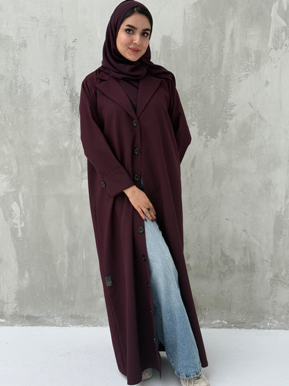 A woman wearing a Maroon Coat-Style Abaya with buttons down the front, paired with a matching headscarf.