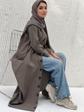 A woman wearing an Olive Green Coat-Style Abaya with buttons down the front, paired with a matching headscarf.