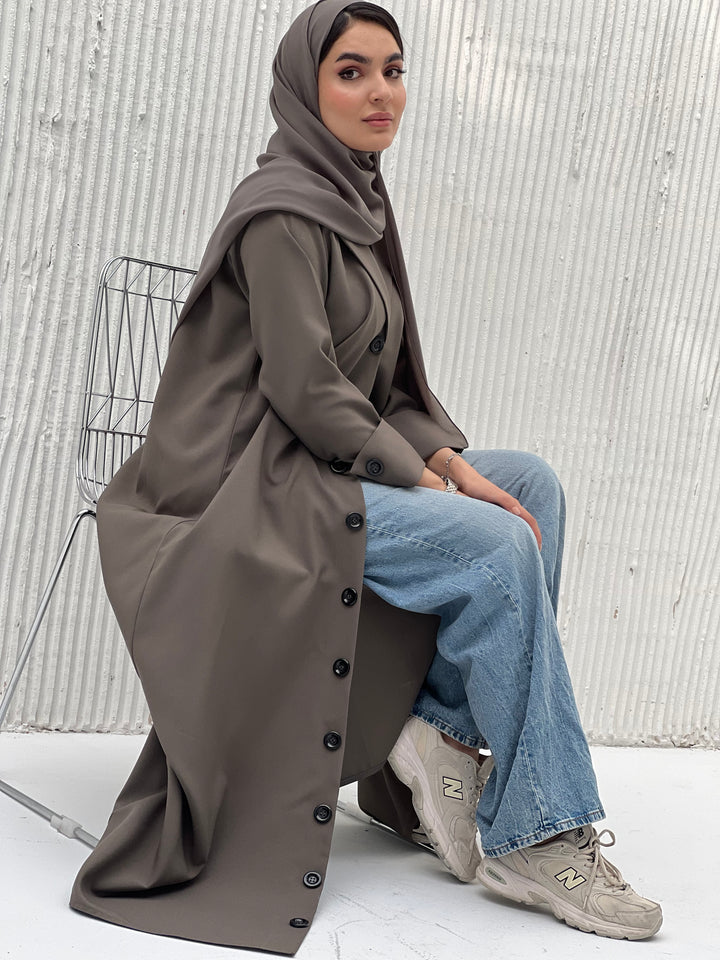 A woman wearing an Olive Green Coat-Style Abaya with buttons down the front, paired with a matching headscarf.