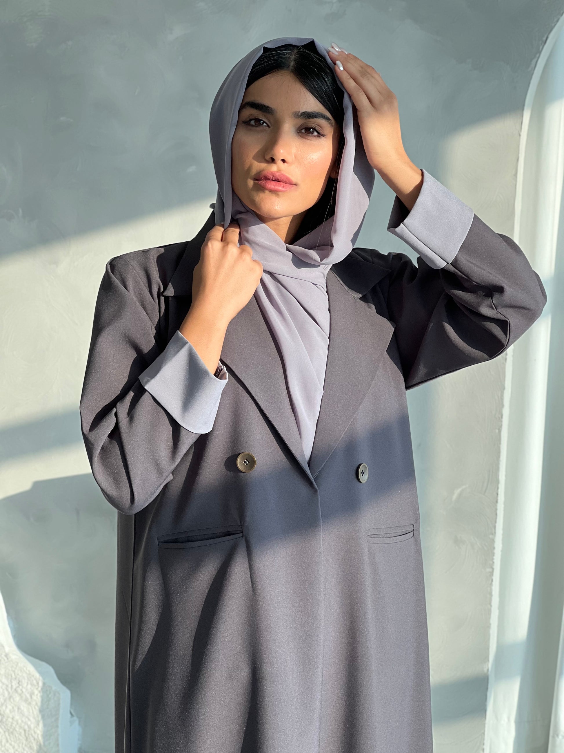 A woman wearing a Slate Grey Blazer-Style Abaya with long sleeves and a matching Sheila, standing indoors.