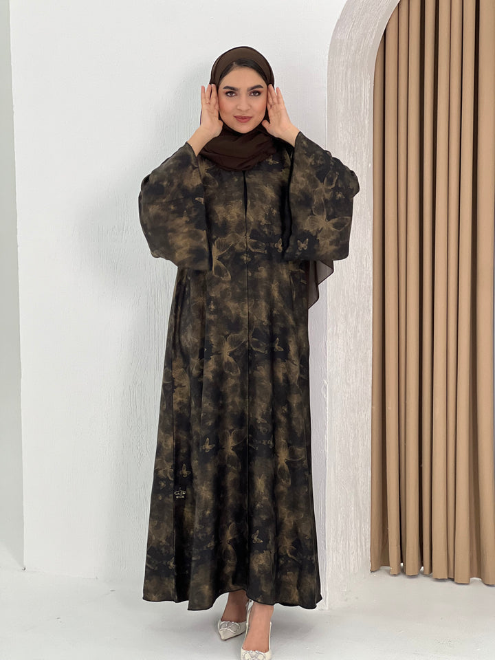 A woman wearing an Abstract Bronze Black Satin printed abaya with long sleeves and a round neckline.