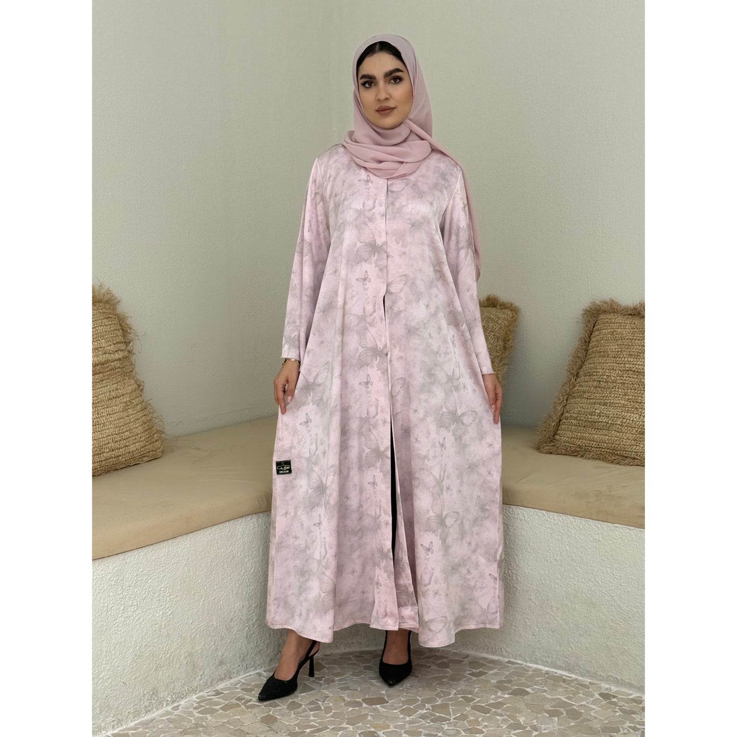 A woman wearing a baby Pink Printed Satin printed abaya with long sleeves and a round neckline.