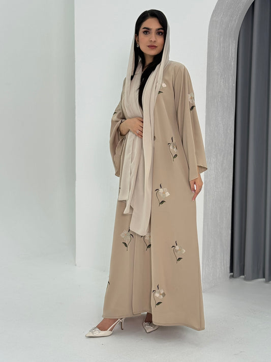 A woman wearing a beige Classic flowy cut abaya with scattered embroidery, floral patterns, and a matching headscarf / Sheila.