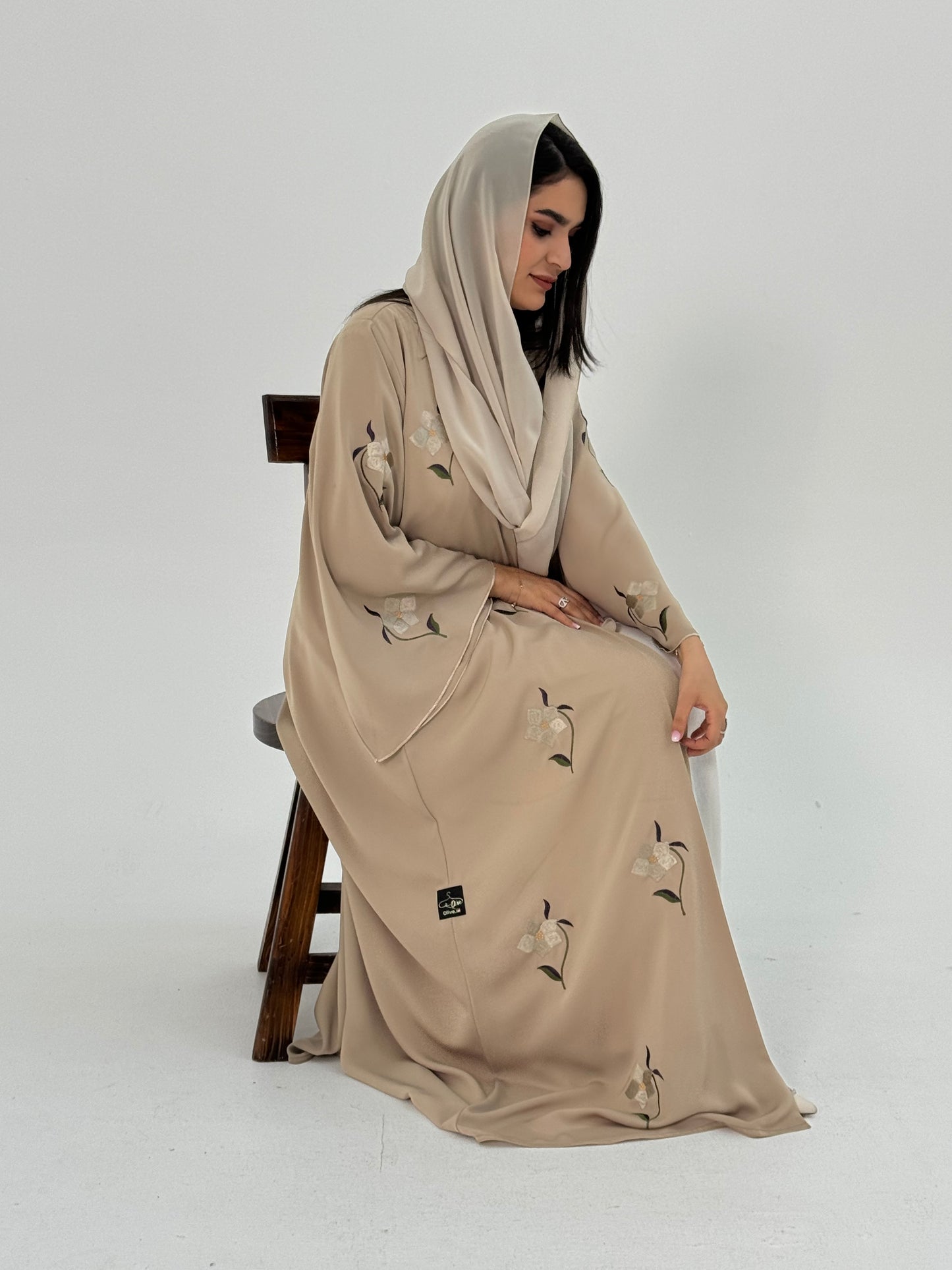 A woman wearing a beige Classic flowy cut abaya with scattered embroidery, floral patterns, and a matching headscarf / Sheila.