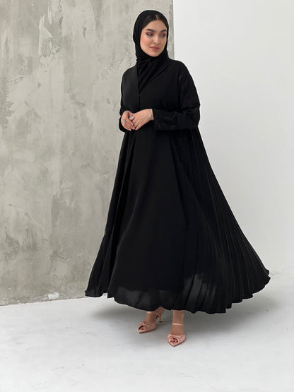 A woman wearing a Black Pleated Abaya with Floral Details, with long sleeves and a matching Sheila, in an indoor setting.