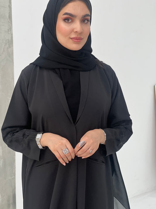 A woman wearing a Black Blazer-Style Abaya with Embroidered Sleeves with a Sheila headscarf.