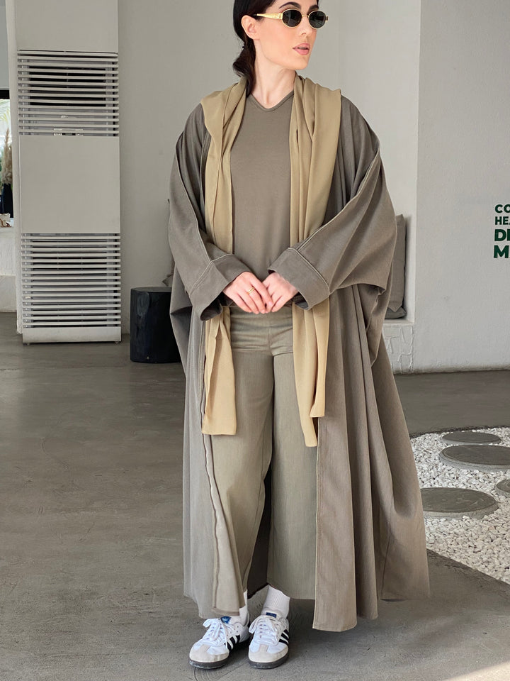 A woman wearing a Grey Cotton abaya with pants and a top, standing in a room with light decor.