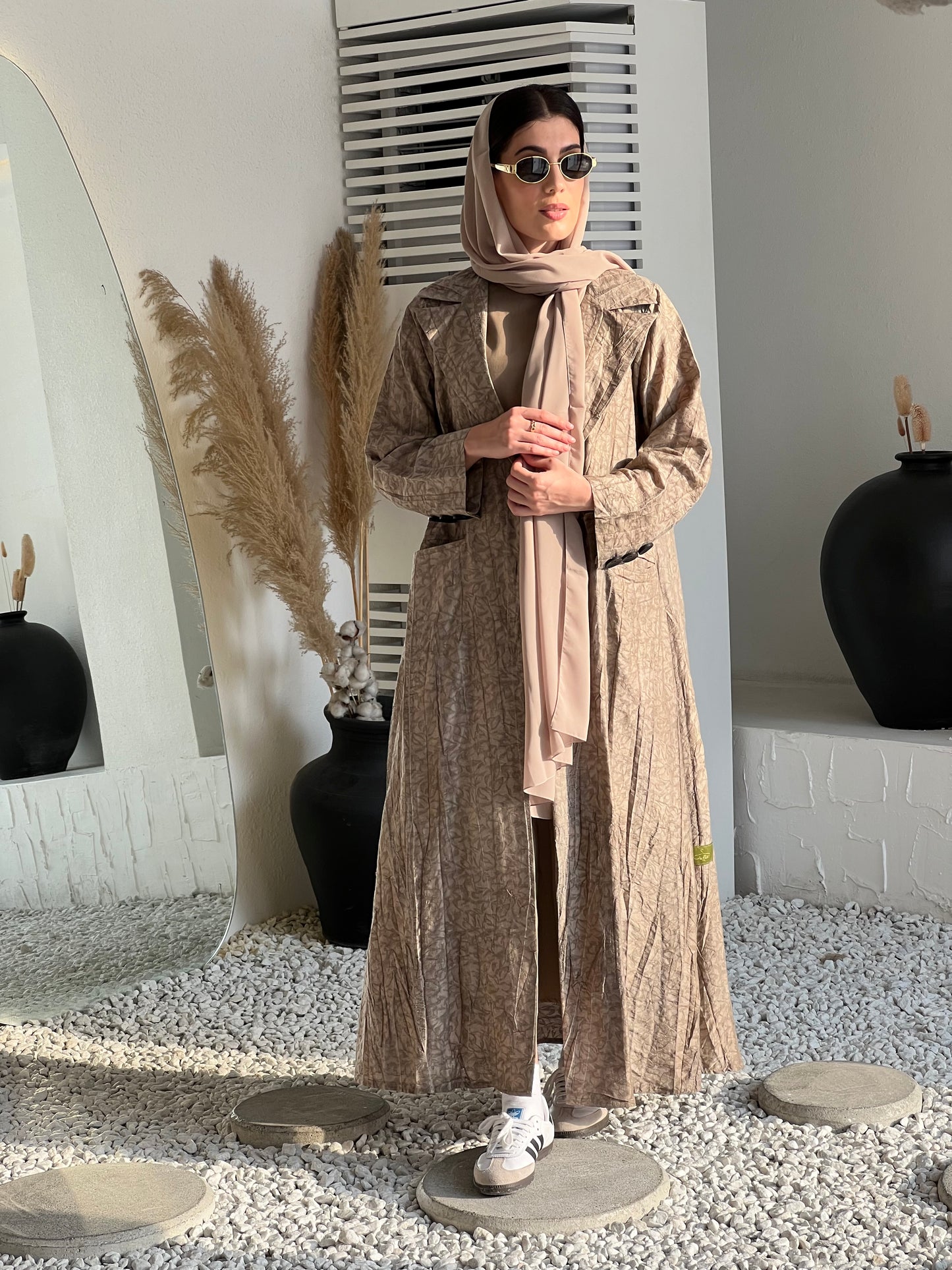 A woman wearing  a Beige Printed Trench coat style with buttons and pockets in an indoor setting
