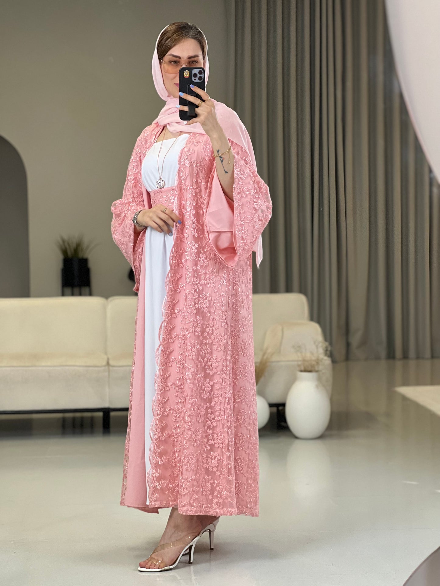 A woman wearing a Pink floral dantel abaya with wide sleeves and a matching Sheila headscarf paired with a white inner dress underneath.