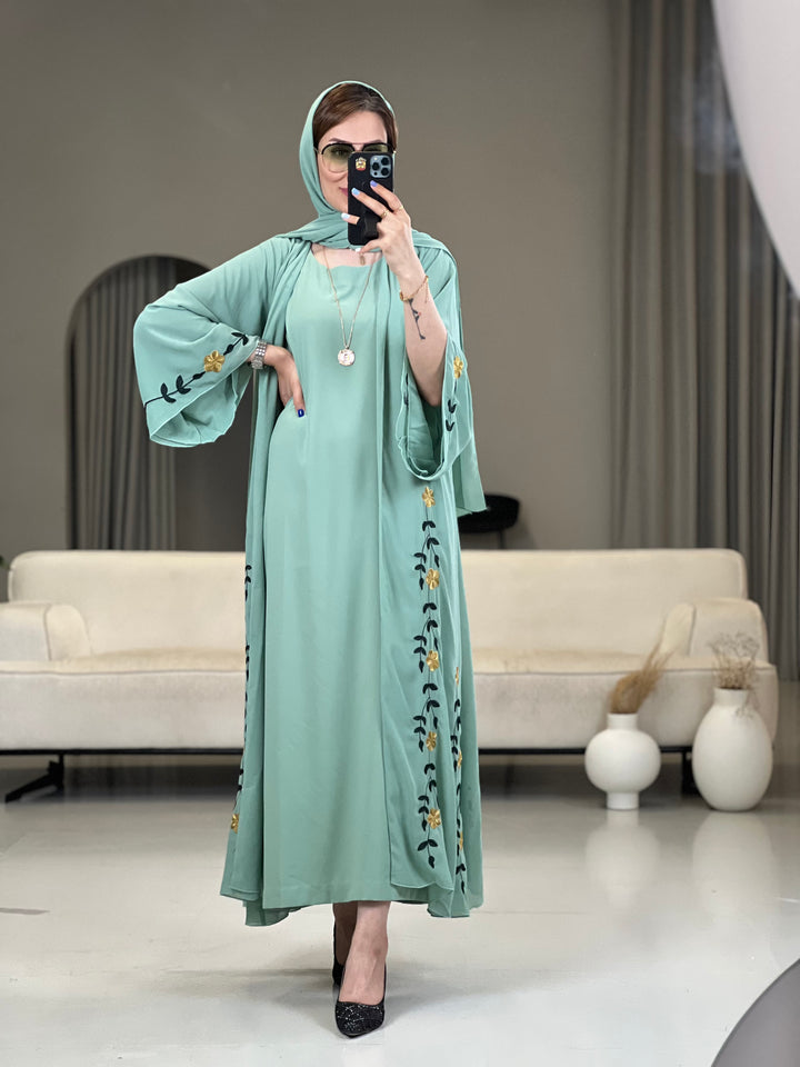 A woman wearing a Mint Green with Black & Yellow floral Embroidery details Open front chiffon abaya with wide sleeves 