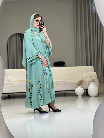 A woman wearing a Mint Green with Black & Yellow floral Embroidery details Open front chiffon abaya with wide sleeves 