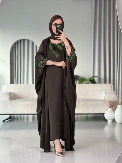 A woman standing in a room with white furniture, wearing a Dark Olive Green with Bright Green Beading satin, Open front abaya style with embellished sleeves and inner and matching sheila