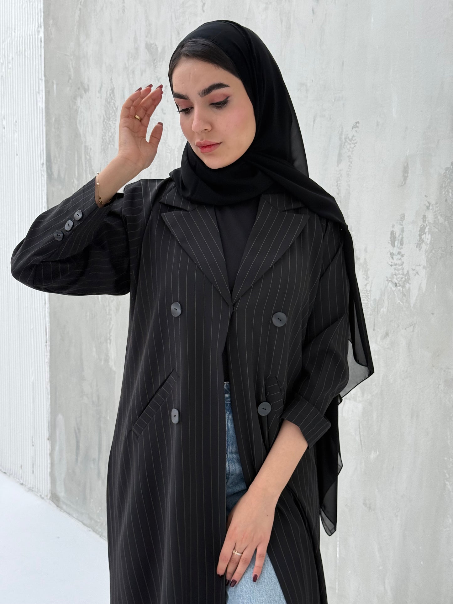 A woman wearing a Black Pinstripe Linen Coat Abaya with a striped pattern, featuring a hood and button-down front.