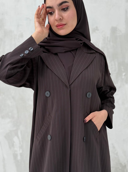 A woman wearing a brown abaya with a sheila, featuring a striped pattern, double-breasted design with buttons, and a V-neckline.