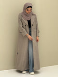 a woman wearing a beige Coat style abaya with lapel collar, Contrast black buttons, large patch pockets, cuff straps and matching sheila